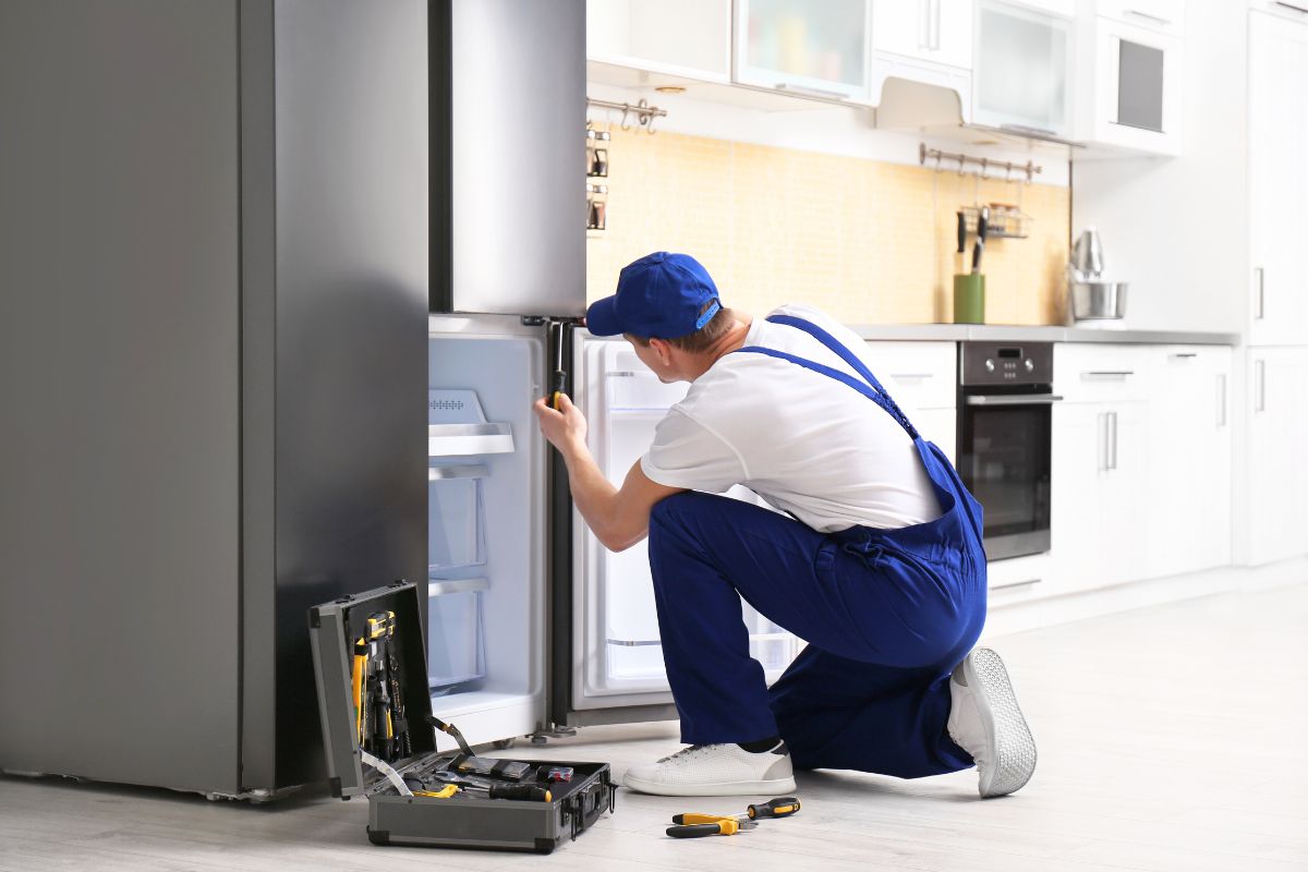 Male technician with screwdriver installing refrigerator on kitchen