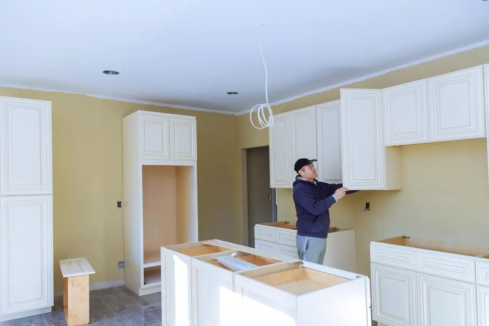 Contractor carefully installing cabinets in a bright kitchen, demonstrating professional craftsmanship.